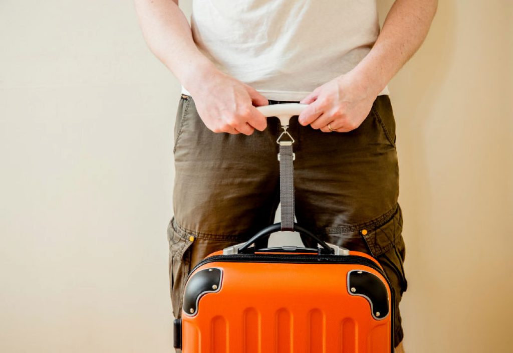 Man tourist using digital luggage scale at home to weighs luggage